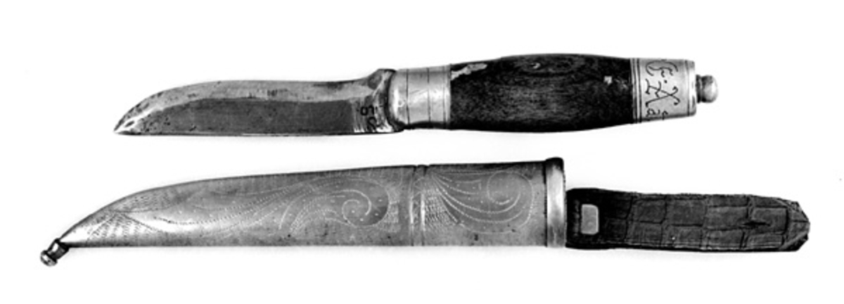 Kniven har brunbeiset skaft, antageligvis av bjørk. Slire og holker er av messing. Slira er foret med papp. Hempa er av imitert krokodilleskinn. Kniven er innkjøpt sammen med andre kniver i ei samling fra Birger Arntzen. 
