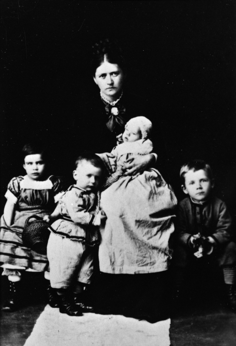 Studioportrett, familiegruppe. Mor med fire barn. Barna er Hagny (piken), Gunnvald, Vilhelm og Ivar. Barnas mor i midten av bildet er Alhed Agersborg Fliflet. En yngre bror. Arne Fliflet ble født i 1875.