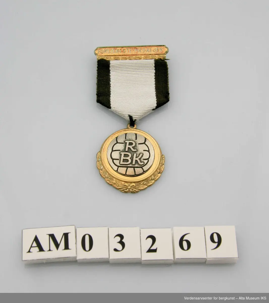Form: Medalje m/løv i underkant, bånd fra ornamentert agraff
Motiv: fotball med RB  innenfor løvkvister m/sløyfe. Svart og hvitt bånd. 