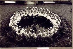 Gruppe, kvinner, uniformer, skaut. Dei sit i ring rundt font