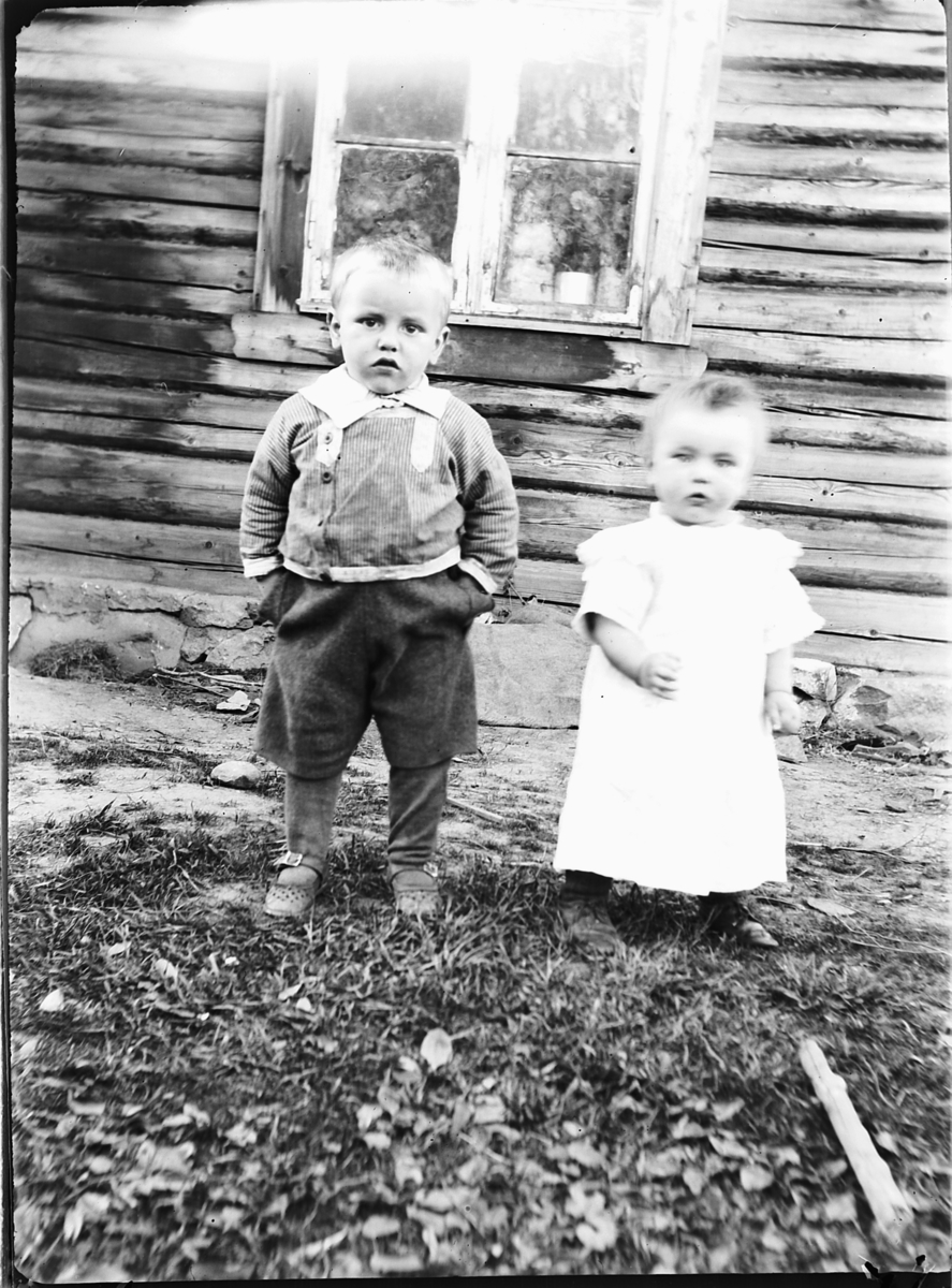 En liten gutt og jente utenfor et hus. 