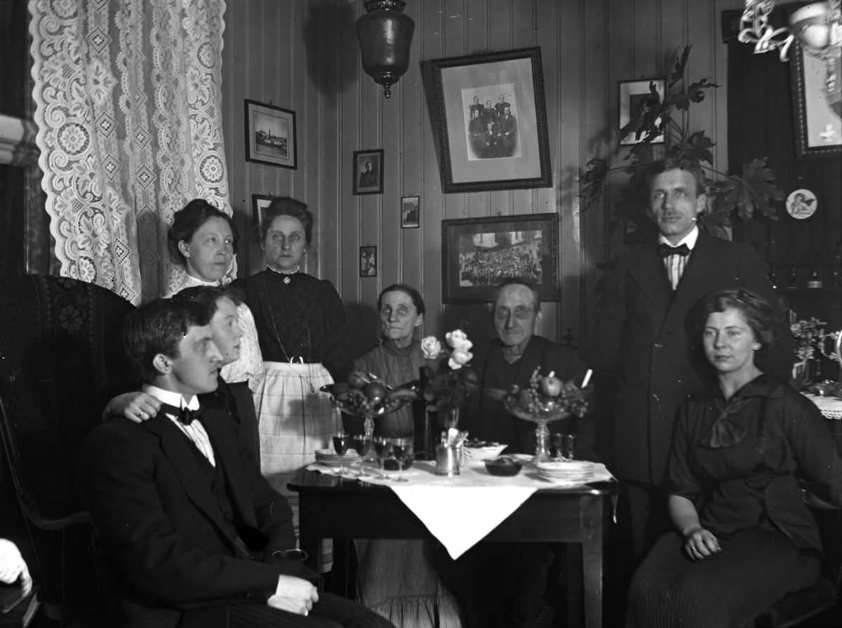 Ukjent familie samlet rundt et stuebord med frukt og drikke. Interiør. 