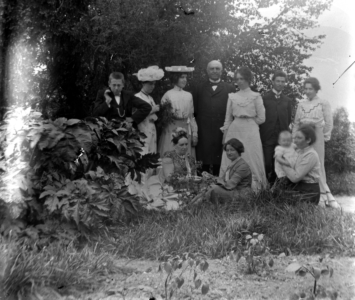Familiegruppe i hagen på Hovinsholm gård, Helgøya i Ringsaker. Ukjente, bortsett fra Anna Hoel gift Ingier, sittende foran til høyre med datter Agnes på fanget. Bildet er fra 1903. Foto Jacob Hoel.
