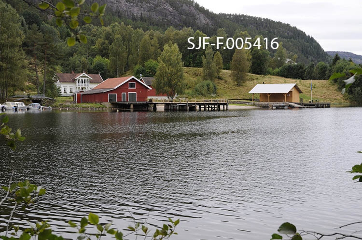 Strengen i Flåbygd (Nome kommune i Telemark), sett fra stranda på nordsida av det trange sundet med samme navn.  Ved Strengen var det brygge, og her hadde dampbåten Axel, som slepte tømmer på Vestvannene (Bandak, Kviteseidvatn og Flåvatn i Vest-Telemark), sin base.  I dag går mesteparten av trafikken i dette området på fylkesveg 107, hvor det i 1964 ble bygd ei buebru i armert betong over Straumen.  Brygga med godshus er imidlertid intakt, og området nedenfor brukes også som fortøyingssted for fritidsbåter.  Fotografiet er tatt fra stranda på nordsida av det trange sundet mellom Flåvatn og det nedenforliggende, kanaliserte vassdraget. 