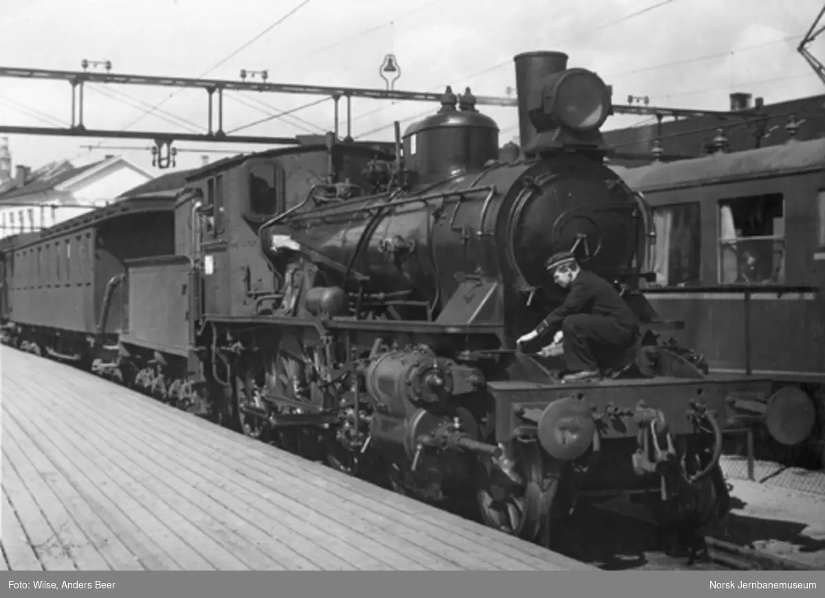 Damplokomotiv type 27b nr. 369 foran persontog på Oslo Østbanestasjon : fyrbøteren eller lokomotivføreren er i gang med smøring