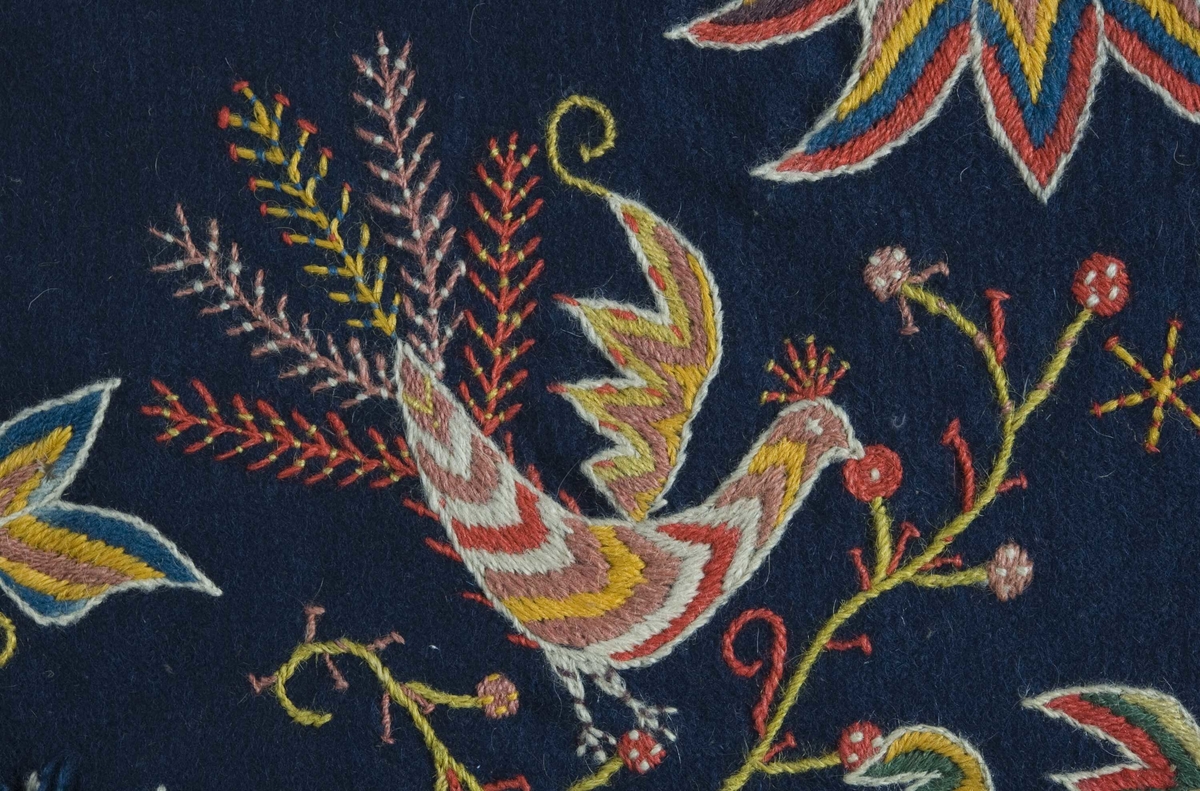 Mørkblå putetrekk med brodert dekor i ull, blomster og fugler.