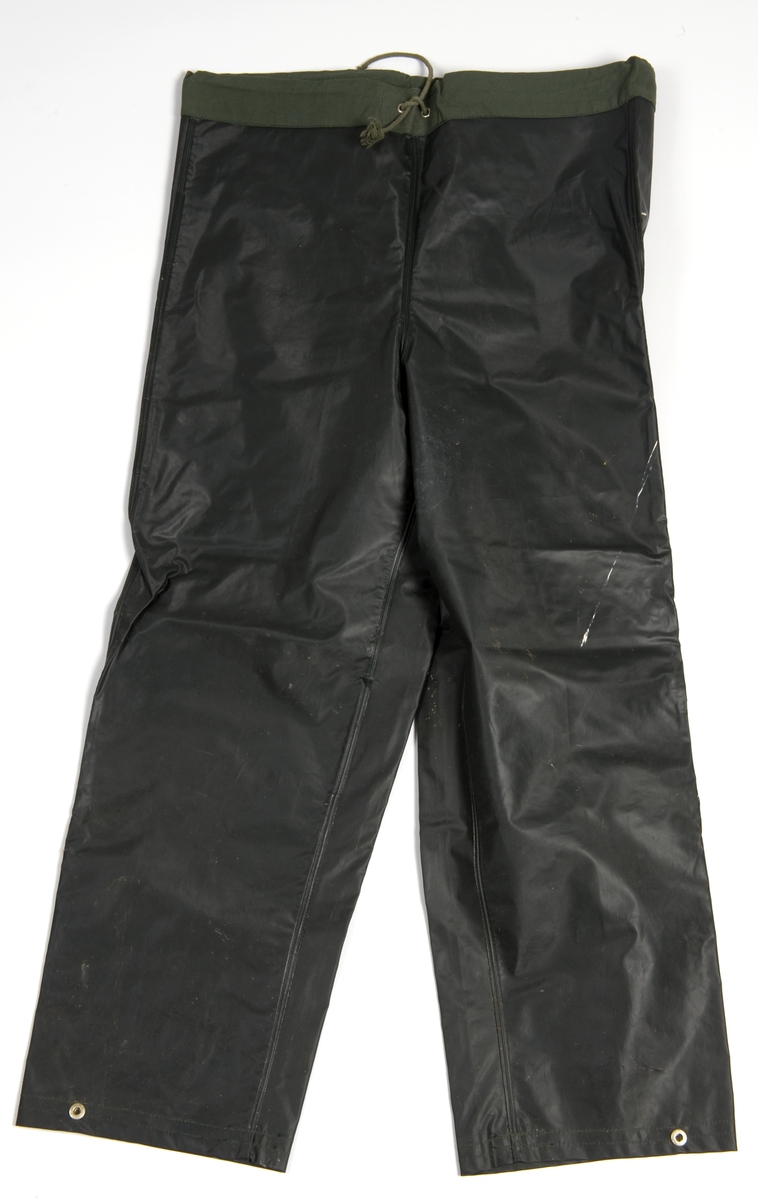 Mørk grågrønn regndress: jakke og bukse + sydvest. Plastbelagt tekstil. 
Bukse med rette ben, løpegang med bomullsnor i livet og ved anklene.
