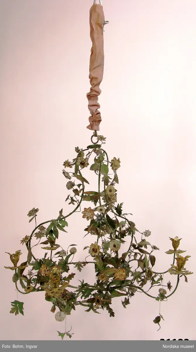 Ljuskrona, rokoko, så kallad lövverkskrona, av klippt och målad plåt. Utformad som ett naturalistiskt lövverk med gröna blad och flerfärgade blommor på en päronformad stomme. Sex svängda ljusarmar med blomkalksformade ljuspipor av förgylld mässing. Kedja för upphängning.
Anm: Kronan konserverades 2013.
/Anna Womack 2015-06-05