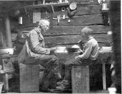 Nils Bjørgum og David Nyre sitter på kasser og spiser i en å