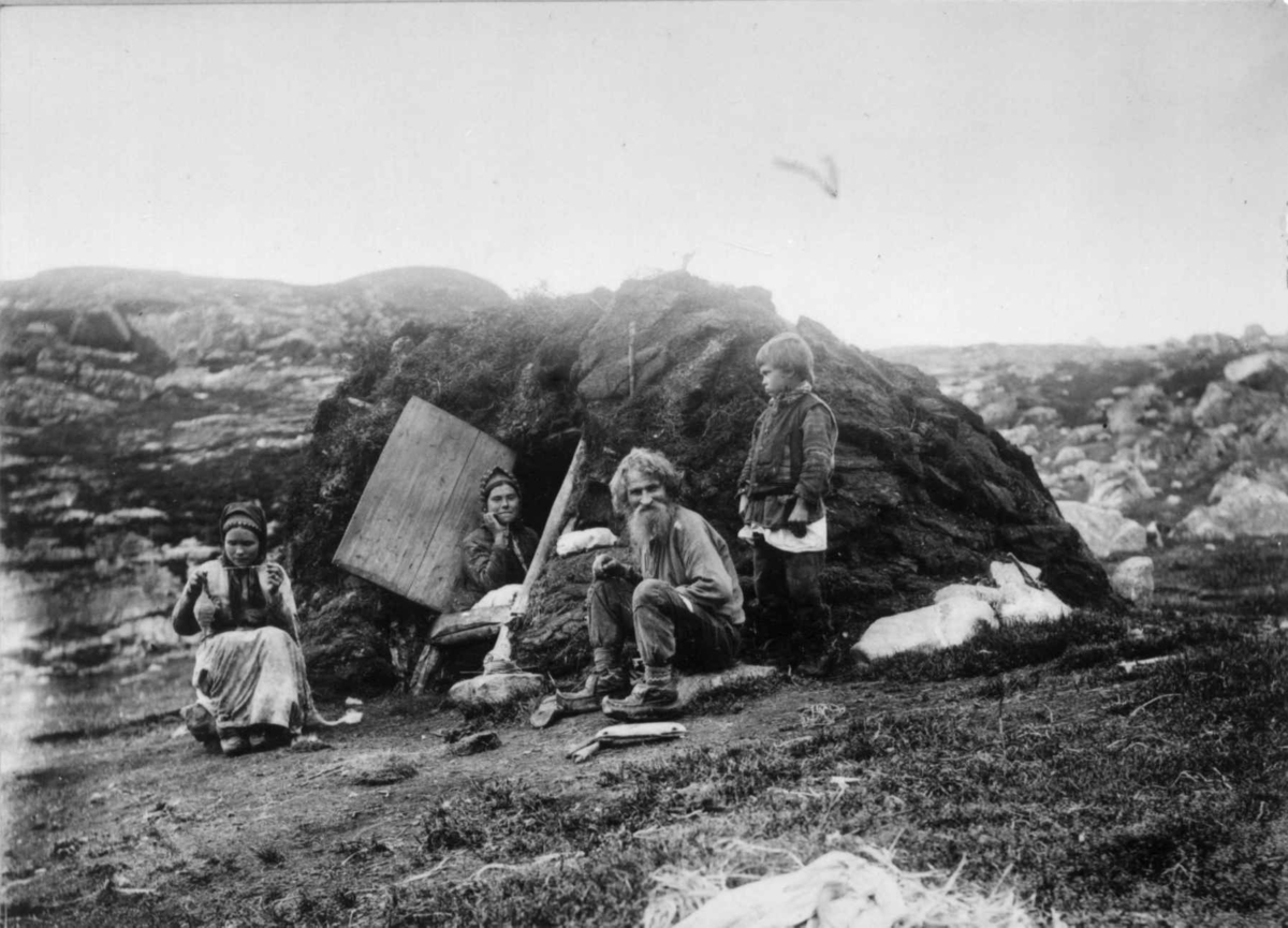 Skoltesamer utenfor gamme. Sør-Varanger, Finnmark, ca. 1900. Kvinnen til venstre spinner på håndtein.