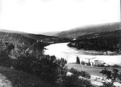 Landskap, ukjent sted. Skogkledd dalområde med elv, veiparti