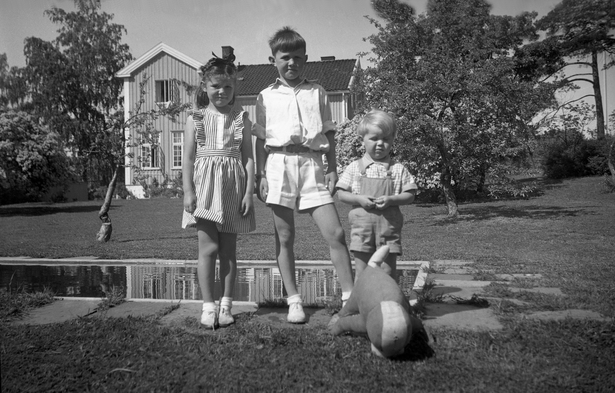 Søsknene Annette, Petter og Carl Artur Solberg står i hagen, nabo av Arentz. Fotografert 1947.