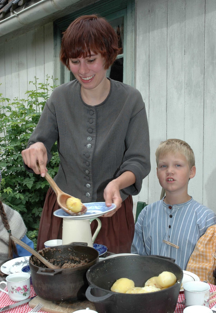Levendegjøring på museum.
Ferieskolen uke 31 i 2005.Kvinne og barn i drakter spiser middag "hjemme" på Enerhaugen på Norsk folkemuseum. 
Norsk Folkemuseum, Bygdøy.