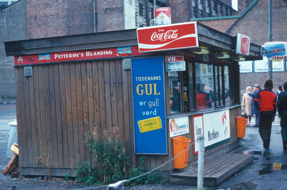 Gatebilde med mennesker og kiosk med reklameskilt for Coca Cola og Tiedemanns Gul.