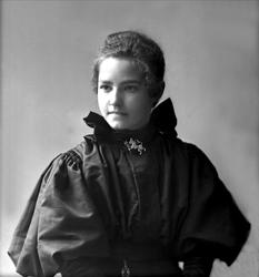 Portrett, Kathinka Andvord i svart drakt, smykke formet som 