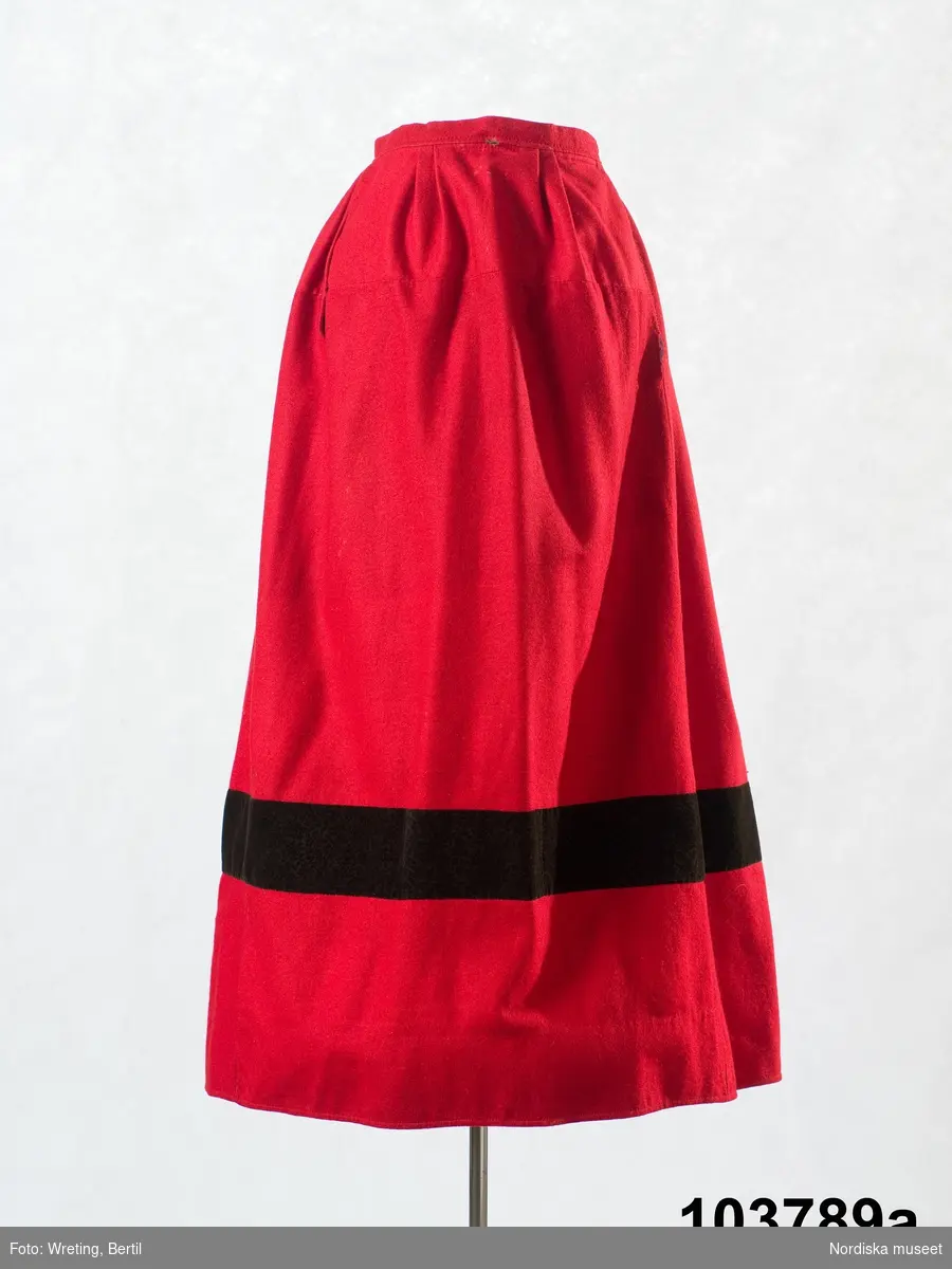 Huvudliggaren:
"Bruddräkt 'bruaklänning'. Bestående av en röd kjol ('bruaskört  '), svart tröja ('bårdetröja') med listeband och vitt förkläde."

Bilaga:

Katalogkort:

c: List.

d: Förkläde: Längd: 79 cm. Bredd: 108 cm. Material: Textil, bomull. Teknik: Manufakturvävning. Handsömnad. Färg: Vit.
Förkläde i vitt manufakturvävt bomullstyg, smalrandigt med små prickar i ränderna, stärkt. Rynkningar mot midjelinning i tuskaftat bomullstyg, 1,5 cm bred, fastsydda bomullsband i sidorna. Fåll nedtill upplagd i sick sack mönster som bildar effektfullt mönster på framsidan. Två lagda veck ovanför fållkant. Förklädet är handsytt.
Lästips: Svensson Sigfrid, (1935). Skånes Folkdräkter, en dräkthistorisk undersökning 1500 - 1900. Stockholm: Nordiska Museets Handlingar: 3.
/Inga-Lill Eliasson 2008-02-20