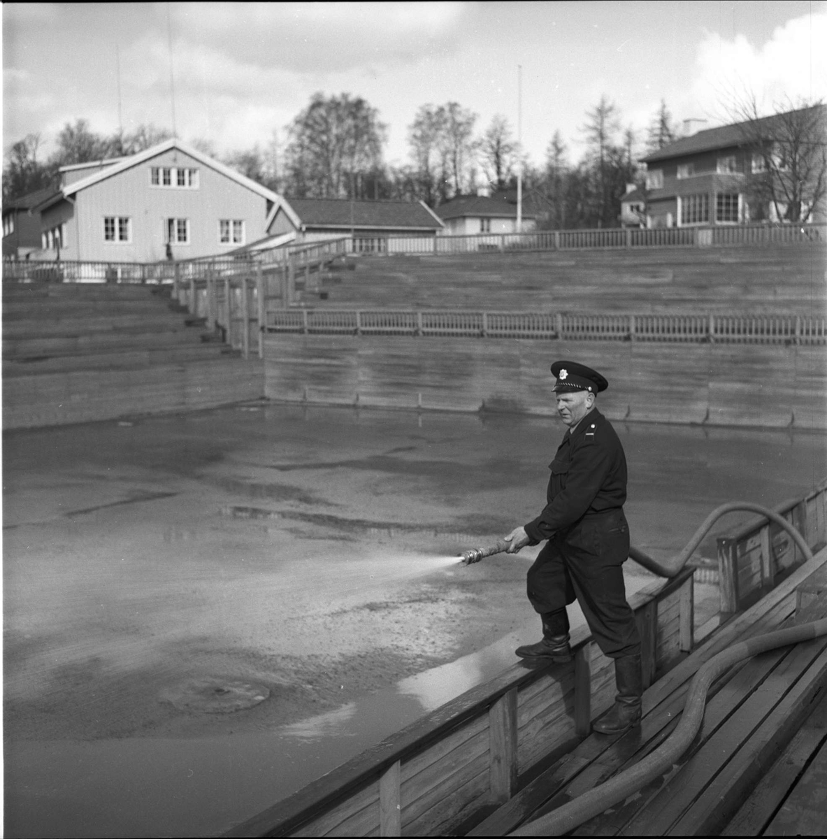 Madserud, Oslo. Menn som spyler idrettsarena med vannslange.



