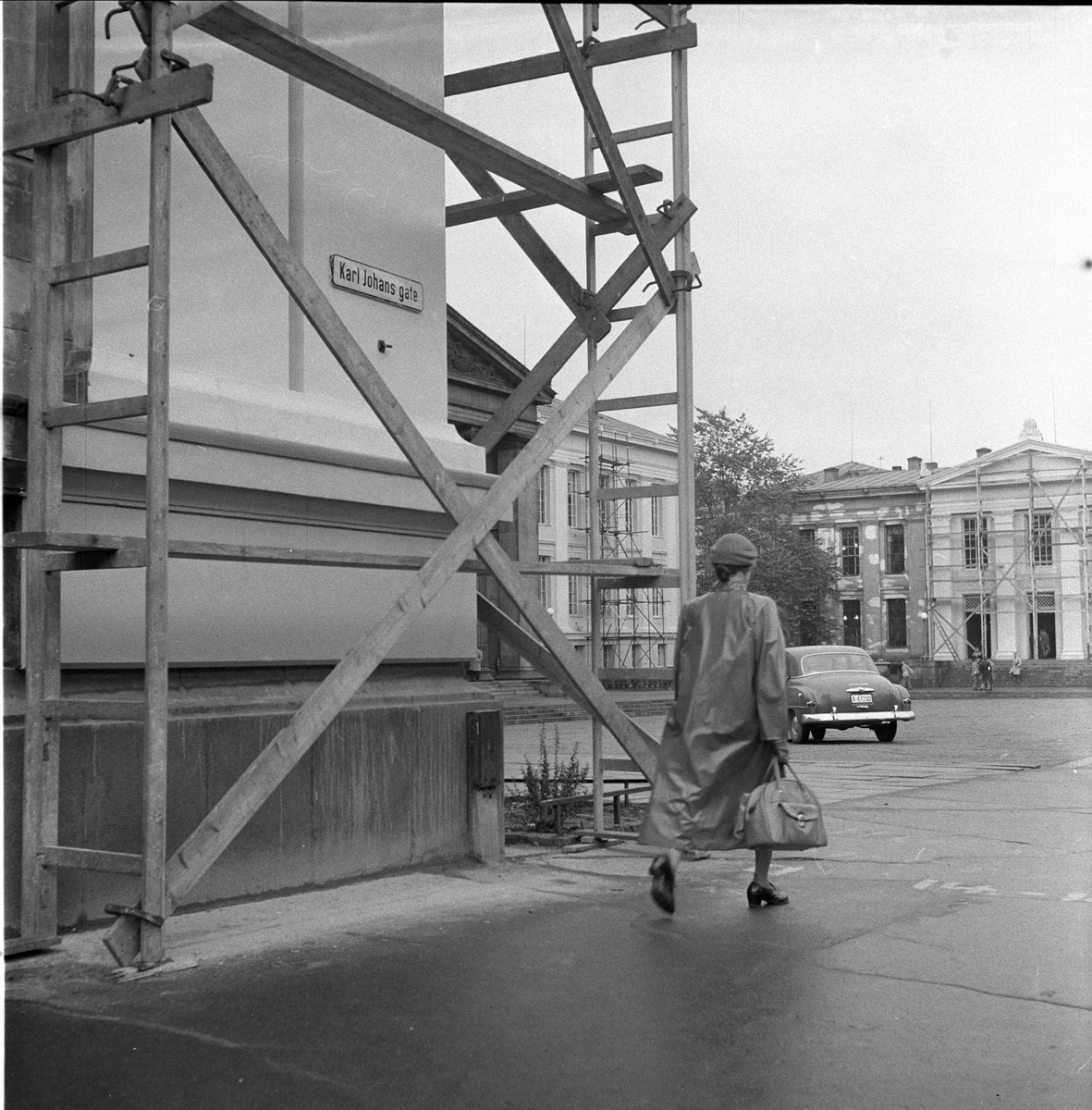 Universitetet, Karl Johans gate, Oslo, 28.09.1956. Byggearbeider. Kvinne passerer.