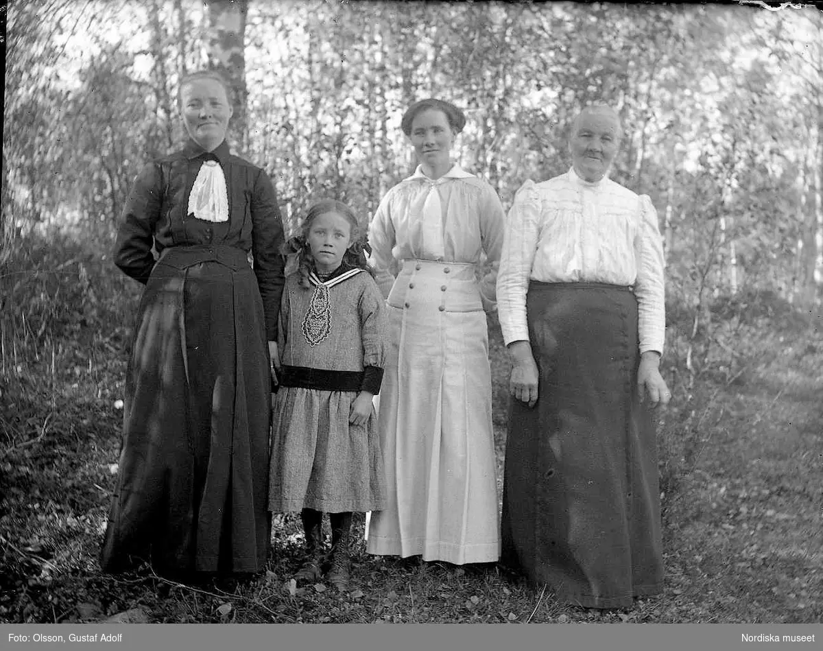 Gruppfoto i helfigur av tre kvinnor och en flicka i det gröna från början av 1900-talet.