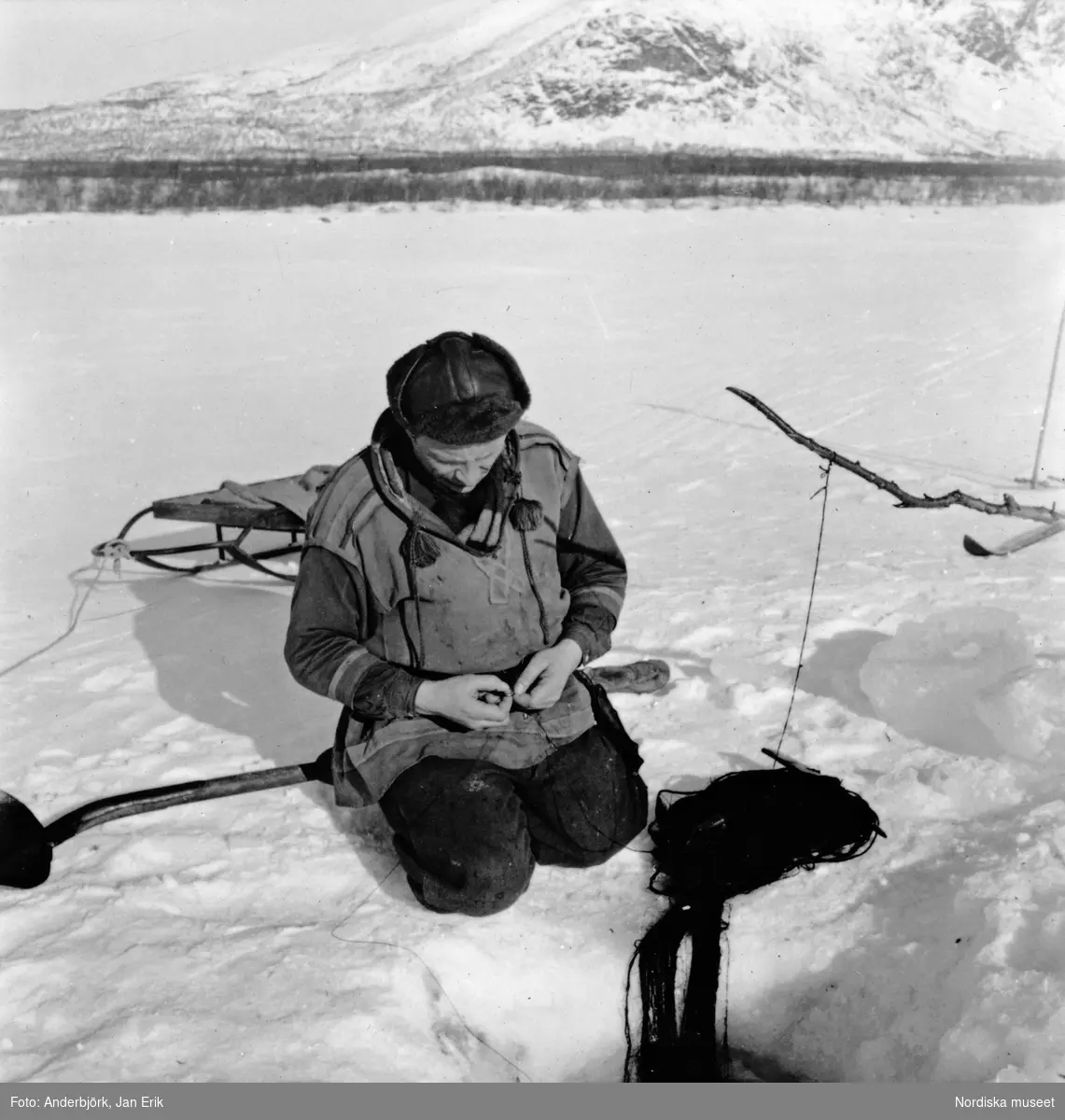 Fiske, Tjuonajokk, Gällivare socken, Lappland. Påskrift på monteringen: "Andreas Labba tar upp nät, som han lagt under isen på Kattumälven. Ingen fångst."