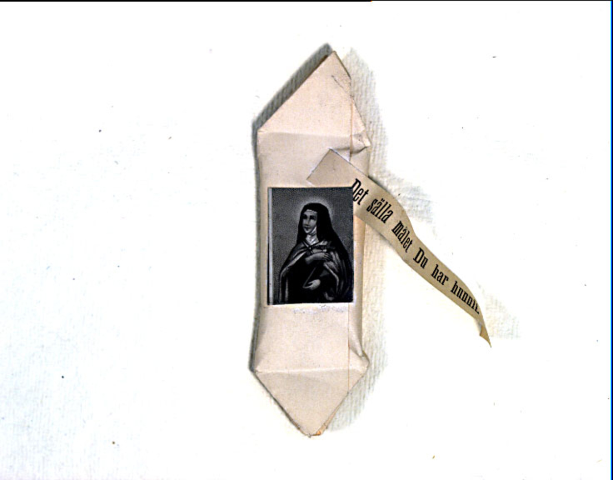Begravningskaramell av vitt papper med svartvit bild av nunna. Textband: "Det sälla målet du har hunnit".