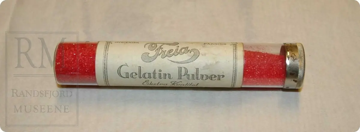 Rødt pulver i glassrør med lokk. Merket mer "Freia Gelatinpulver". På lappen står også oppskrift.
