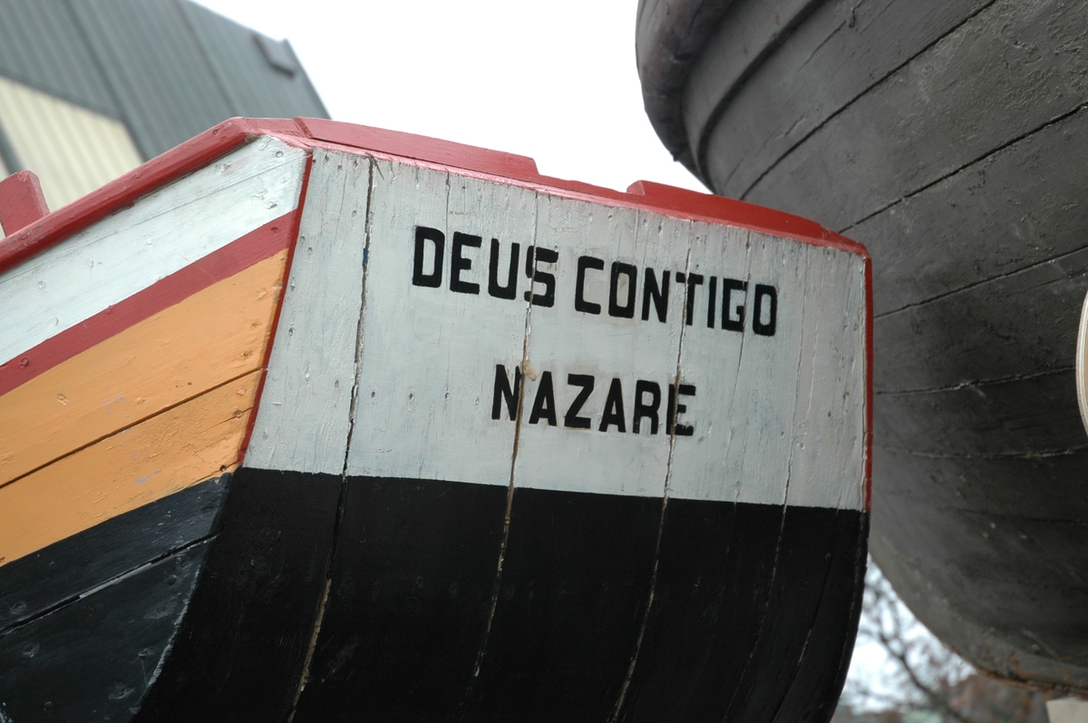 Liten portugisisk robåt med flat bunn, spiss og høy baug. Innvendig sort bunn, blå tiljer/tofter, rød esing mm. Utv. sort bunn, oker, hvit med røde streker, blå.