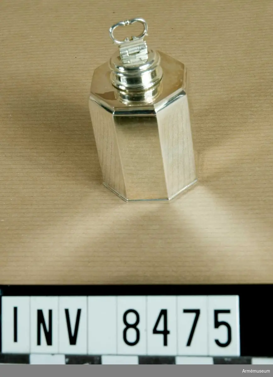 Vinkanna i miniatyr i silver. Gjord efter förebild AM.08249. Märkningar i botten av kannan: GAB tillverkarstämpel, årsbokstav är F 10 1977, silverkvalitet 830, silverstämpel (S) och trekronorstämpel det vill säga kontrollstämpel.

Kannan är 8-kantig med 12 mm kanter. Flaskhalsen är 10 mm bred och gängad för att hålla ett lock. Kannan är inte förgylld som orginalet och har ej heller någon inskription.

Vid tillverkningstillfället kostade kannan 1640 kronor + moms 23.46 % och fanns då i upplaga om 675 st.

Angående orginalvinkannan historia se föremålsbeskrivning AM.008249.