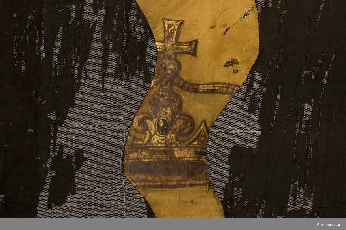 Duk av svart sidentaft med flammor av gul taft. Endast fragment av det målade motivet återstår. En bepansrad arm samt en krona.