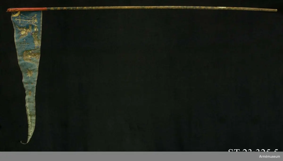 Duk av blå kinesisk sidendamast med målad dekor. Motivet föreställer den romerske kejsaren Konstantins vision av ett kors i skyn kvällen innan slaget vid Pons Mulvius år 312 e Kr mot Maxentius. En ärkeängel med svärd i handen (Gabriel?) svävar över den halshuggne Maxentius. Denna händelse ses som förklaring till att kristna kors började användas på militära fanor. Närmast stångsidan är också ett Golgatakors avbildat. Över detta syns ett moln där Kristus är avbildad. 
Strumpa av rött linne.