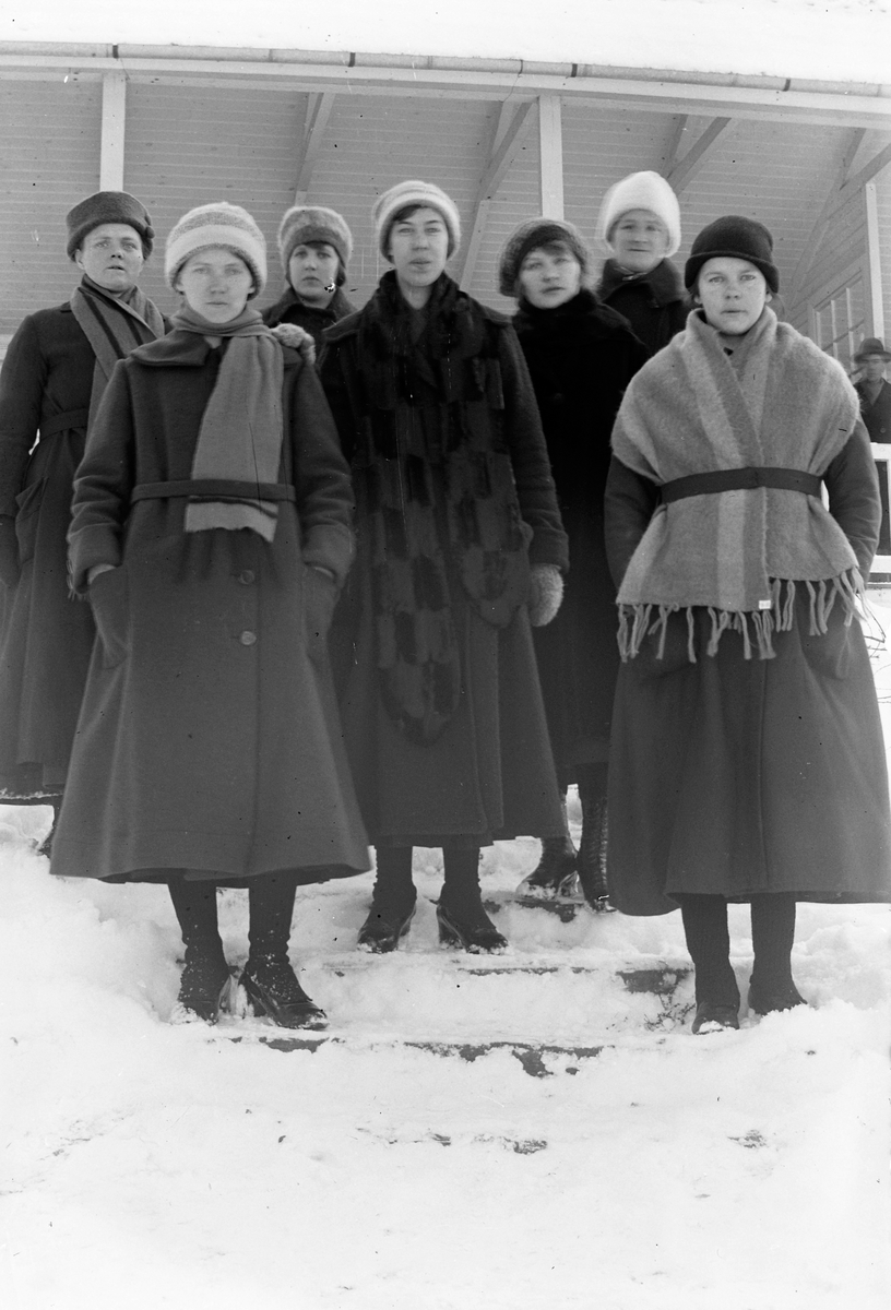 Sju vinterklädda kvinnor står i en snöig trappa, i bakgrunden en träveranda.  Lungkliniken, Eksjö.