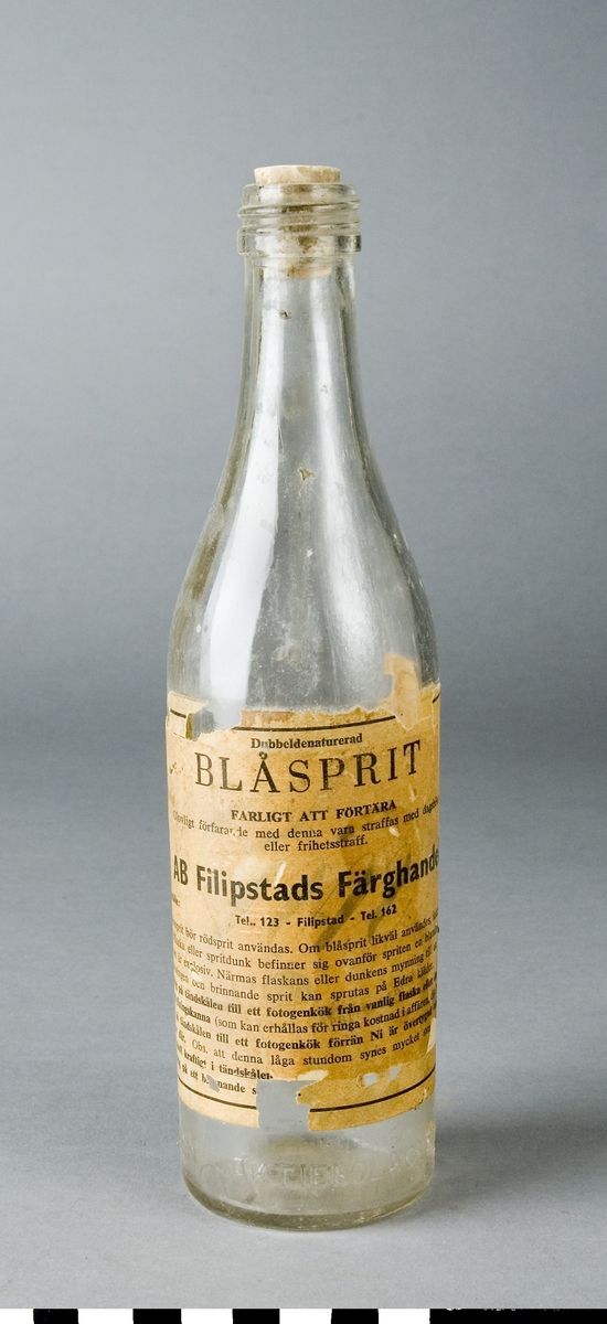 Flaska av klar glasmassa med kork som sitter fast. Utan innehåll.
Med pappersetikett: "Blåsprit" av AB Filipstads Färghandel.
Text i glaset: AKTIEBOLAGET VIN - & SPRITCENTRALEN.