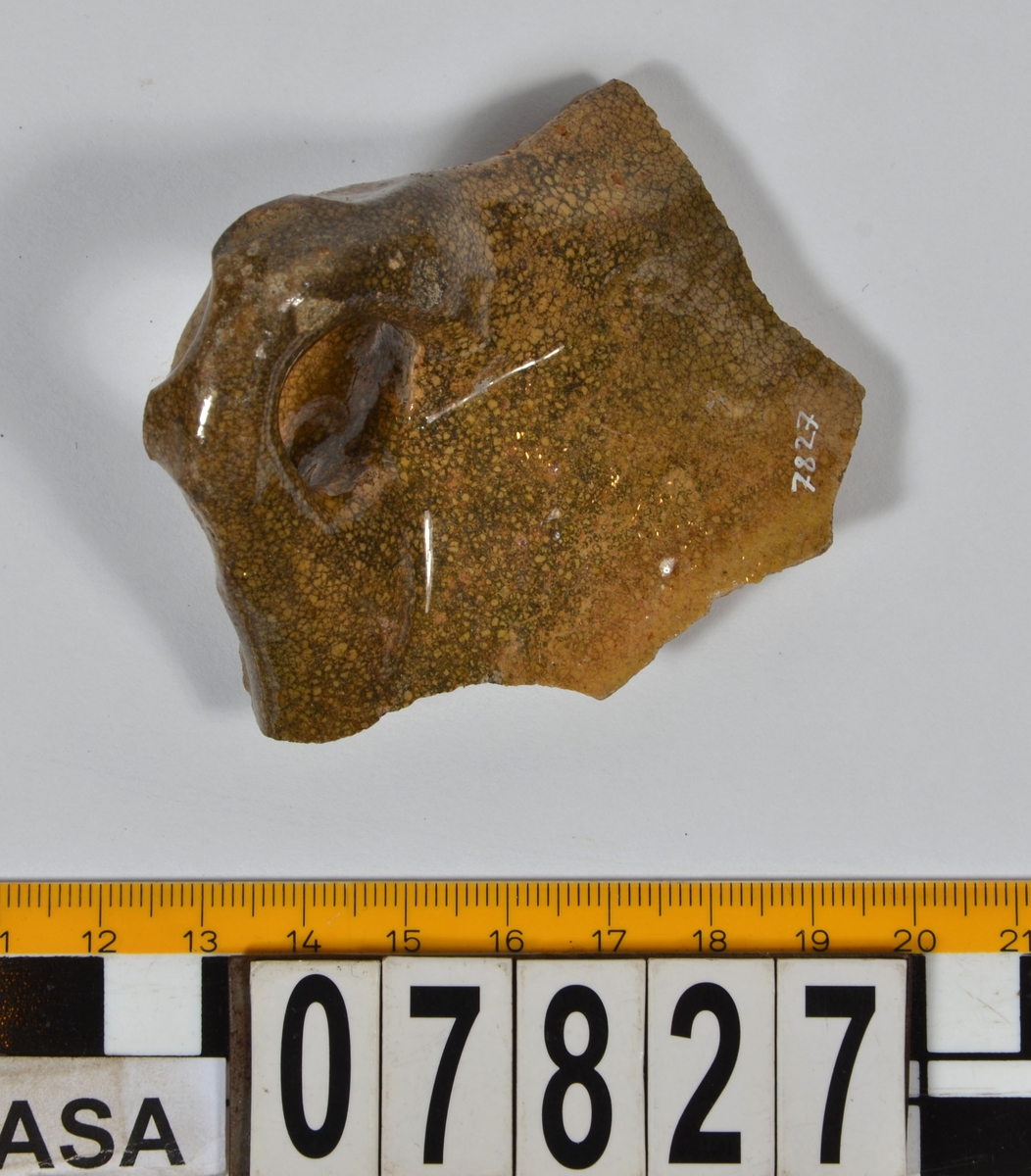 Del av skål.
1 st vertikal bandhänkel, tummad, 70 x 60 mm. Fragment av mynningsrand och buk. In- och utsida blyglaserad gulgrön.