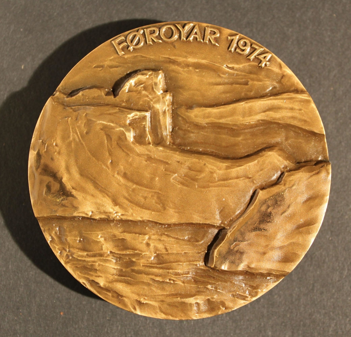 Medalj i brons, rund, kallad "Faerömedaljen 1974. Utförd
avSven Havsteen-Mikkelsen. Åtsidan visar utsikten i Lopra
medBeinisvörd samt text enligt MRK. Frånsidan visar utgrävda
grunderfrån fem kyrkor samt konstnärens signatur. Svart etui
ochmedaljstativ medföljer.