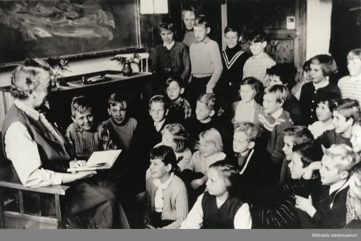 Läraren Elsa Spetz läser sagor för sin klass på Kvarnbyskolan (f.d. Centralskolan). Eleverna sitter och står på golvet framför fröken.