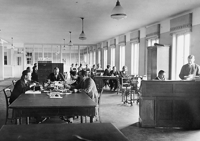 Den första bokföringssalen. Till höger vid skrivbordet kontrollör
N.S. Billing (sittande) och kontrollör M.G. Landahl. Vid bordet till
vänster herrar från Postsparbanken, fr.v. postassistent V.H. Gren,
E.G.B. Ahlstrand, T.R.F. Lindstedt, K.O. Lindman och T.I.A. Rudberg.