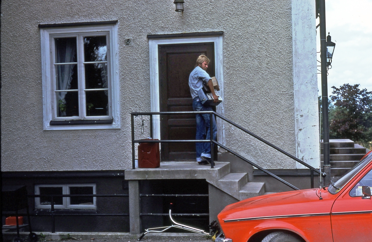 Lantbrevbäraren Mikael  Mattsson vid Hacksta Gård. Han står uppe på trappan, utanför dörren med post under armen. I förgrunden ser man den röda bilen.