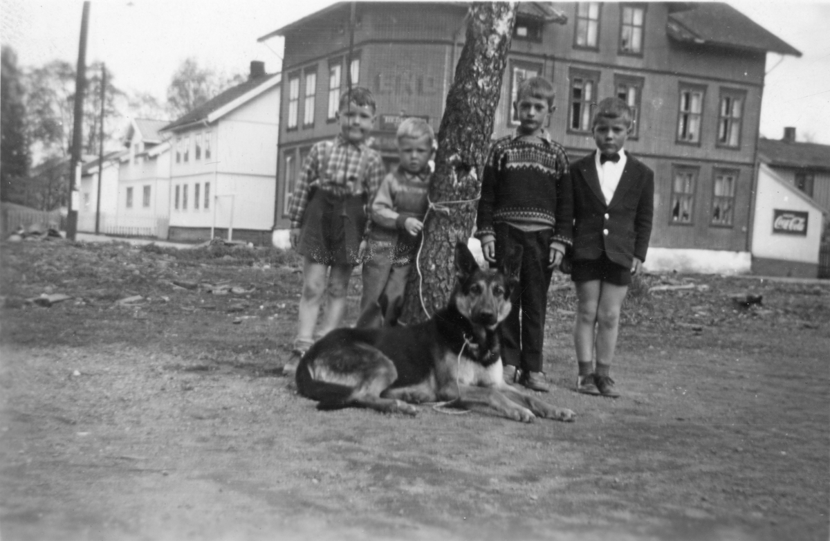 Fire gutter og en hund utenfor Brandvoldboligen. Larsegården i bakgrunnen.