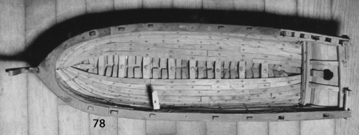 Skrovmodell av fartyg från 1700-talet, grovt tillverkad. Utförd med spant, bordläggning, garnering och uppbyggd galjon, men utan däck och rigg. Akterspegeln sönderbruten. Gulmålad på friborden, vattenlinjen och relingen svart, vit i botten, galjonen brun och insidan av relingen en röd rand.
