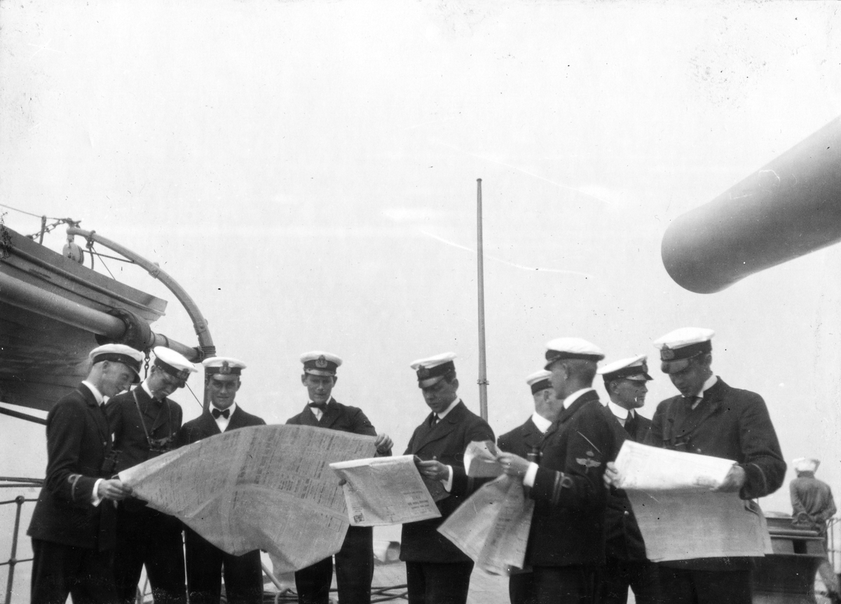 Nio män i uniform läser tidsskrifter på fartygets kanondäck.