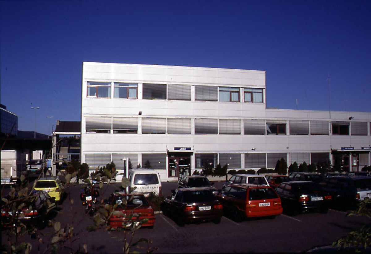 Lufthavn, flere kjøretøyer står på 1 parkeringsplass foran 1 flyplassbygning.