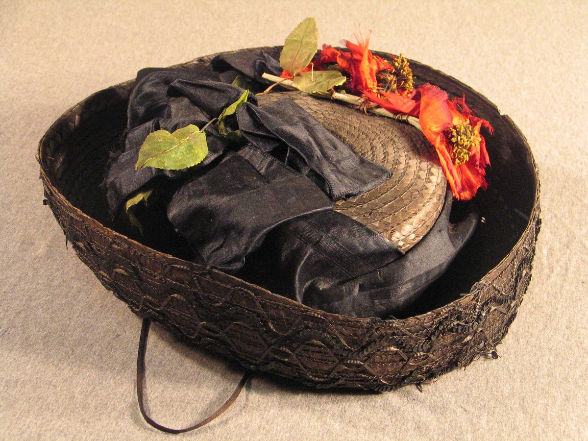 Stor svart silkesløyfe rundt pullen, raude silkeblomster, grøne blad av voksa papir. Bremmen er dekorert med svarte paljettar, stråband og netting.