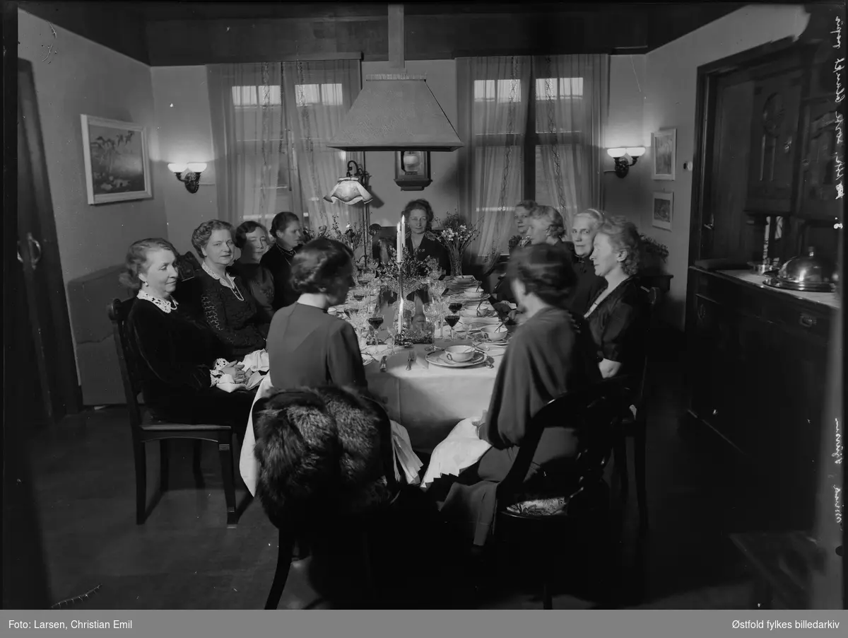 Kvinner festkledd rundt dekket bord til festmiddag i stue. Ukjent sted og personer. Negativ merket Mina Sjursen.