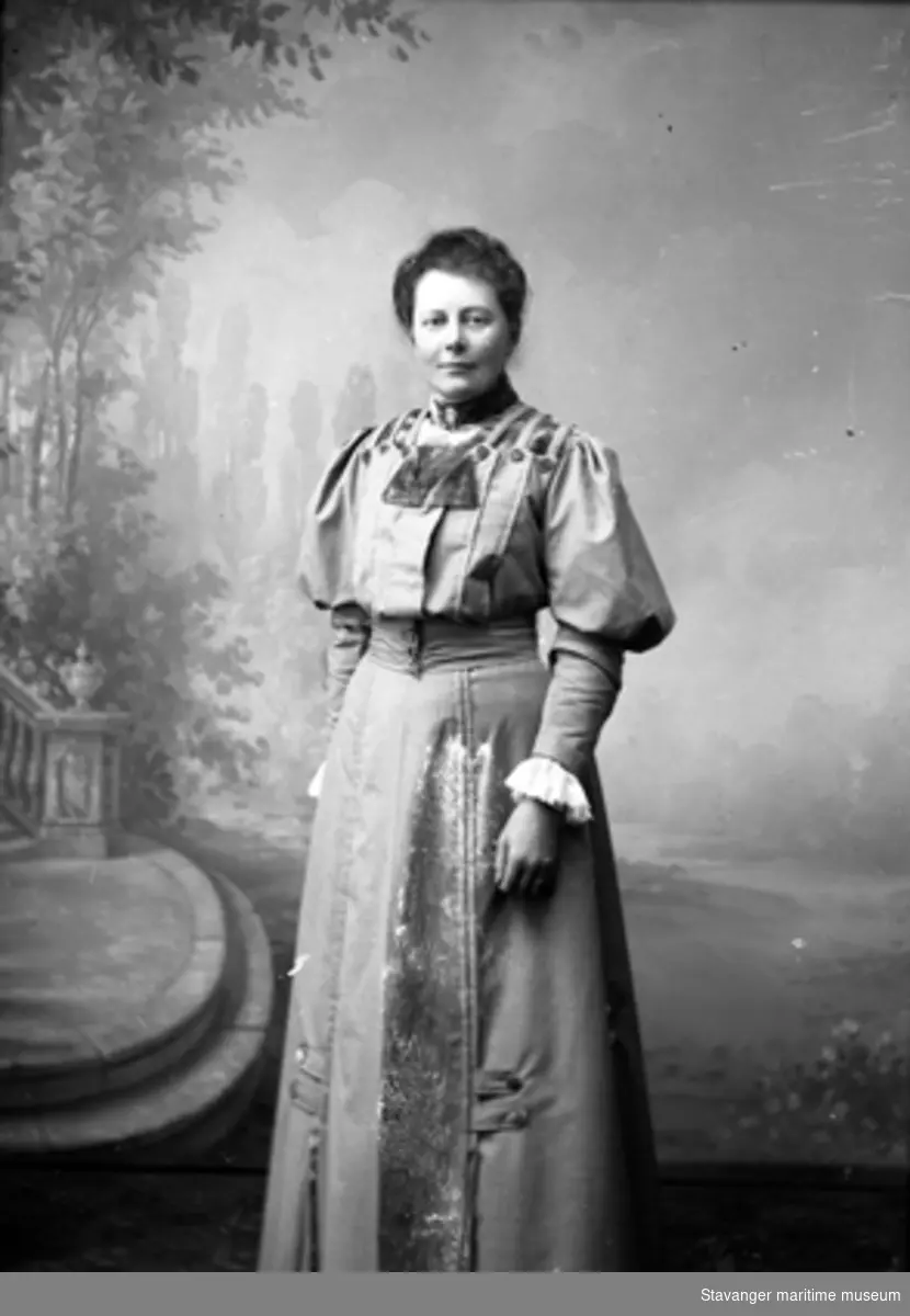 Studioportrett. Helfigur, lys kjole med puffermer. Tatt i atelieet til fotograf Berg i Florø. Julie Lund ca 1905-1910.