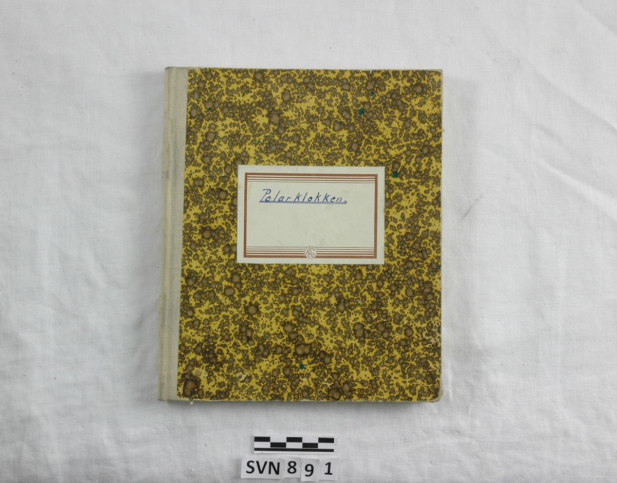 Innbundet notatbok med stiv perm. Mønstrete omslag i brunt og gult. Tekstil på ryggen. Etikett på forsiden, "Polarklokken" skrevet på med penn.