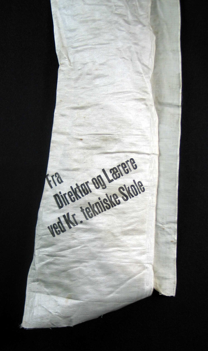 Begravelsessløyfe i hvit silke med svart tekst.