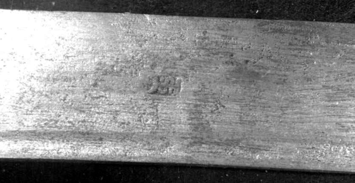 Rund tønneformet knapp i tre. Asymmetrisk feste med tre sidebøyler som har fortykninger på midten på utsiden og tommelbøyle og to sidebøyler på innsiden. Nyreformede parérplater. S-formede runde parérstenger med fortykkede avslutninger på endene. Fremre parérstang er nyere.
Tregrep med jerntrådvikling.
Enegget krum kline med smal ryggstillt blodrand. Smedmerke på venstre side. Klingespissen er dekorert med tre små hull.