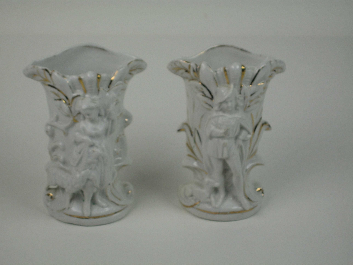 Porselensvaser med dekor i form av bladverk med gullkonturer. Den ene har en framstilling av en gjetergutt med hund og den andre en gjeterjente med et lam.