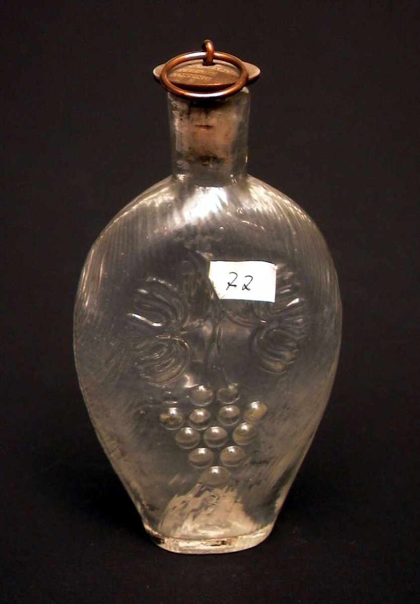 Jaktflaske med buet, flat korpus. Den er dekorert med en drueklase på den ene siden, på den andre en løve. Flasken har kork med metallbeslag. På beslaget står det 'Gustaf VI Adolf Sveriges Konung'.