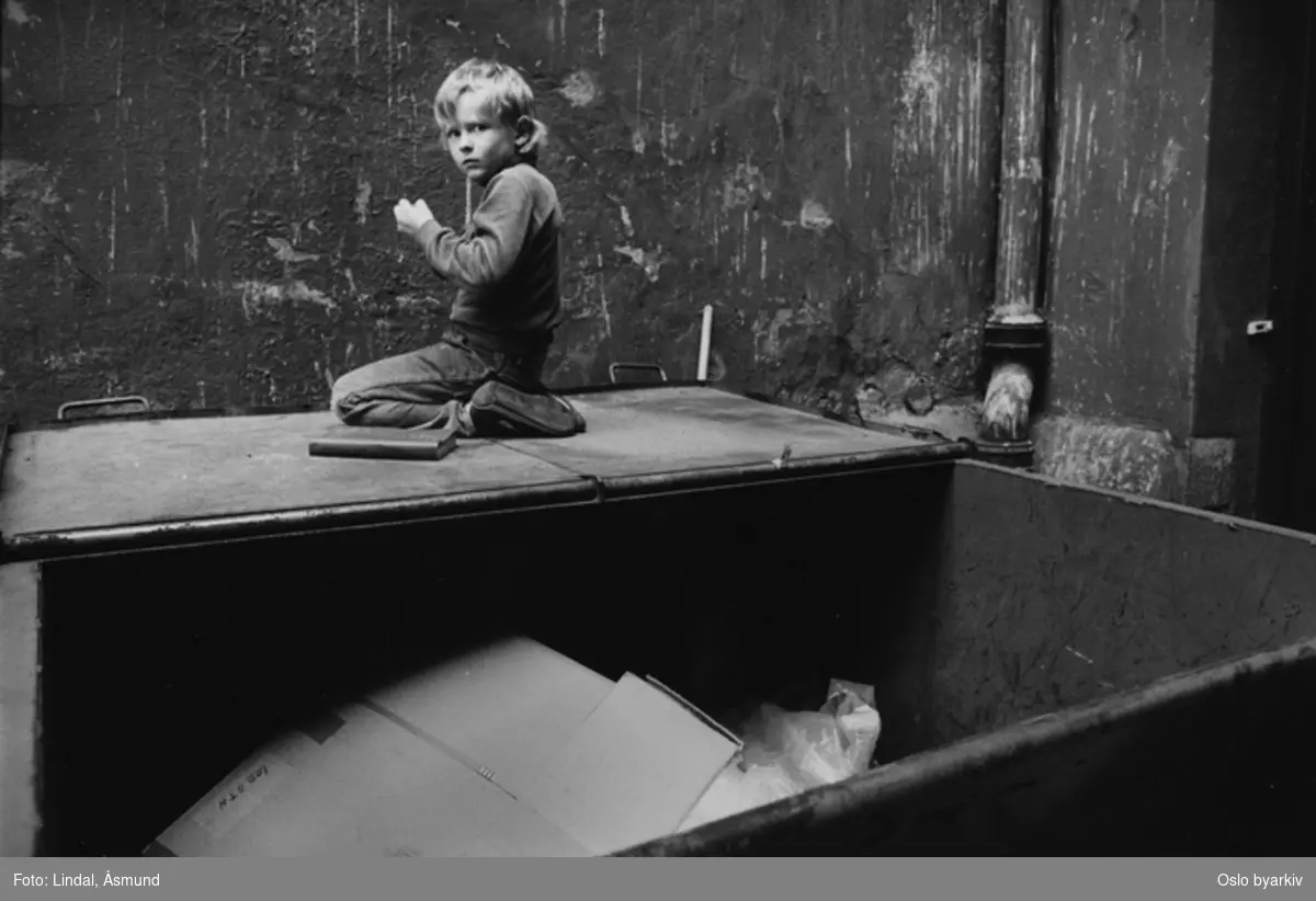 Gutt som leker oppe på en åpen søppelcontainer. Med bakgården som lekeplass. Fotografiet er fra prosjektet og boka ''Oslo-bilder. En fotografisk dokumentasjon av bo og leveforhold i 1981 - 82''. Kontakt Samfoto ved ev. bestilling av kopier.